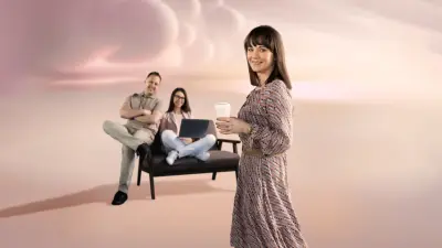 Dwoje pracowników siedzi przy jednym biurku przed swoimi monitorami podczas sesji zespołowego 